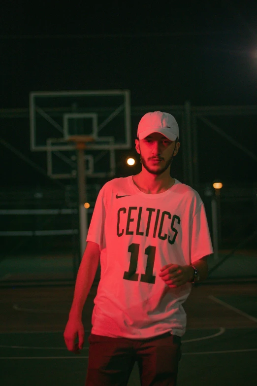 young man in basketball uniform with the hoop at night