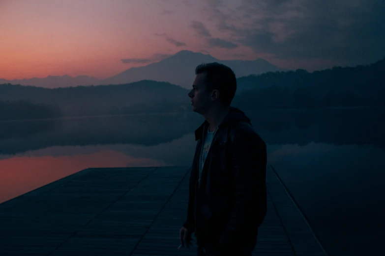 a man stands near a lake during the sunset