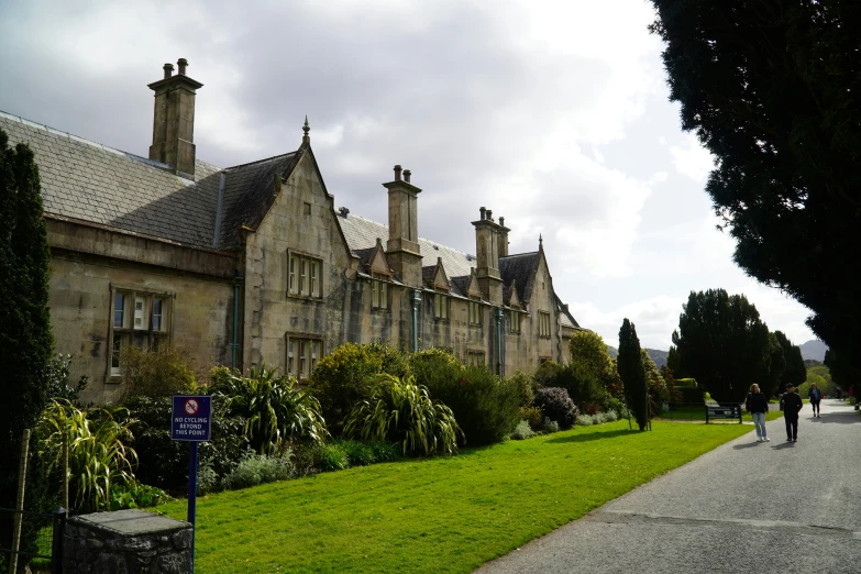 people walking by an old stone building on a cloudy day