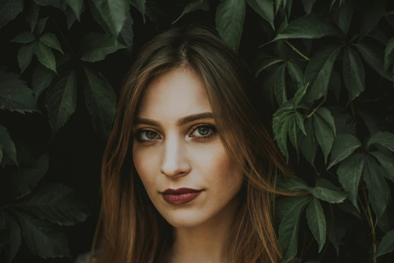 a woman standing in front of leaves with her eyes wide open