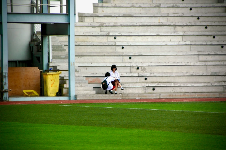 two people sitting on a bench in front of a soccer field