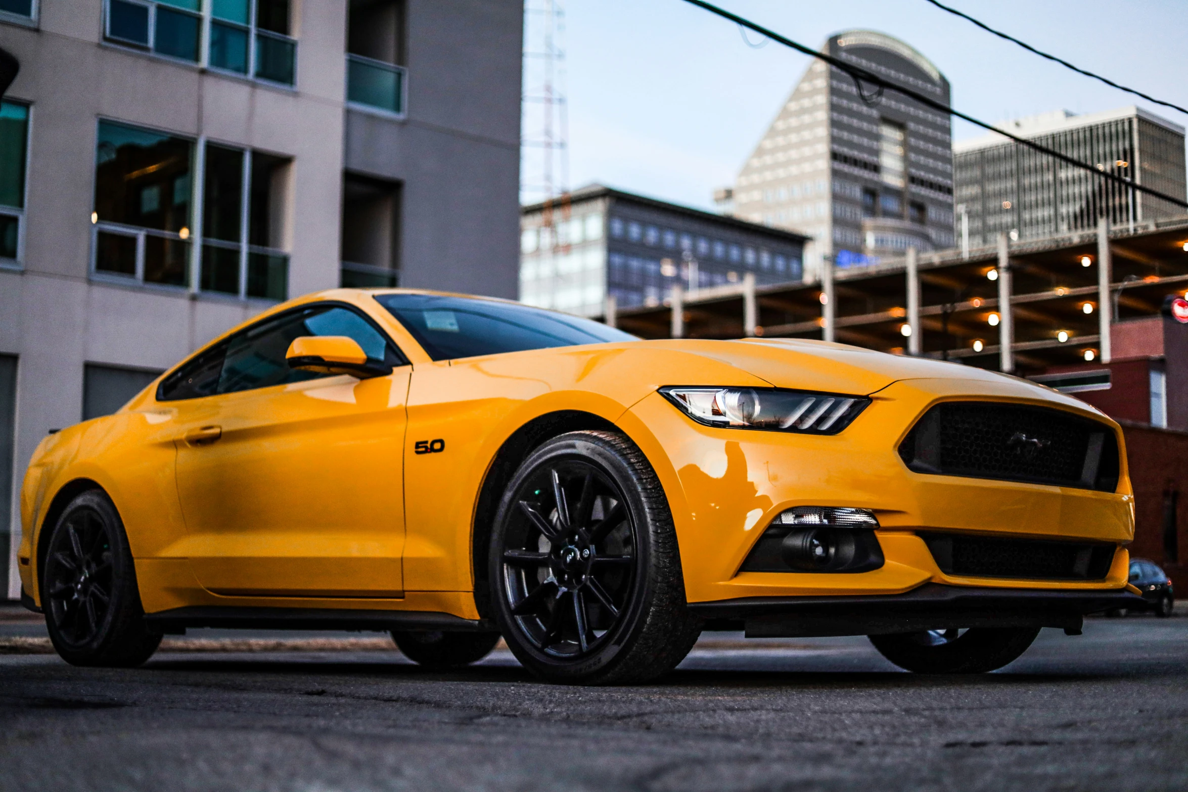 a yellow mustang sits parked on the side of a street