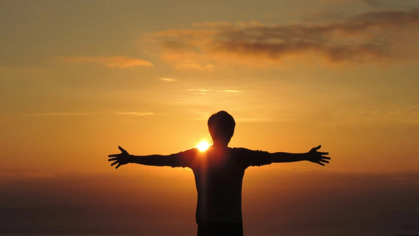 the man is arms outstretched as the sun sets