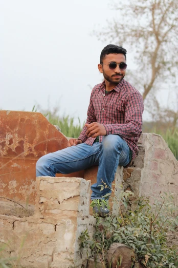 a man wearing jeans and sunglasses sitting on a wall