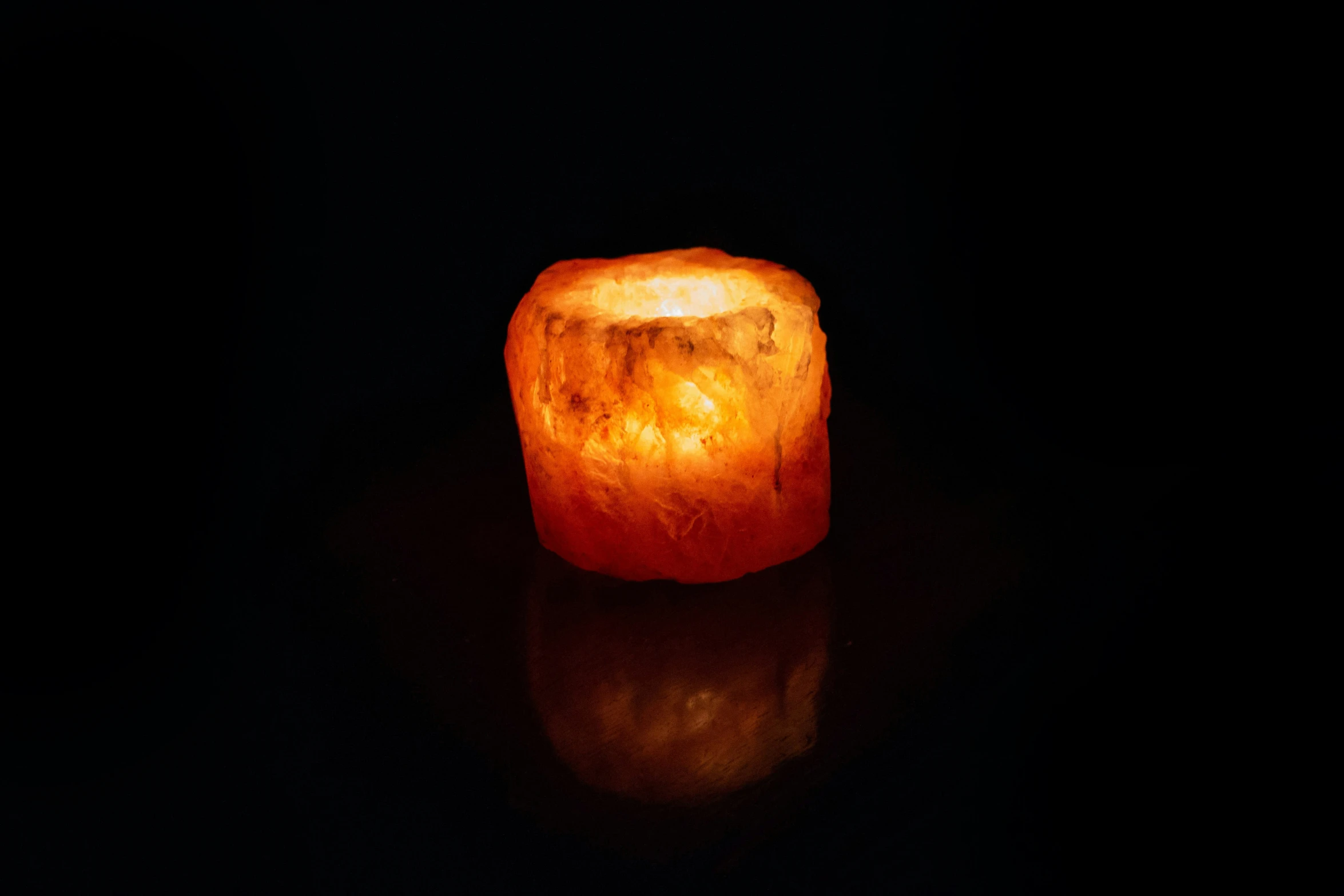 a lighted orange candle sitting on top of a dark floor