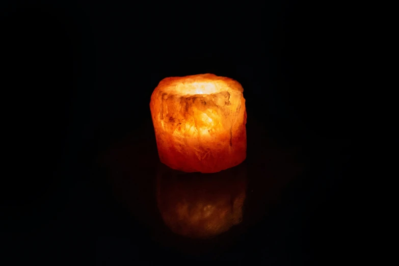 a lighted orange candle sitting on top of a dark floor