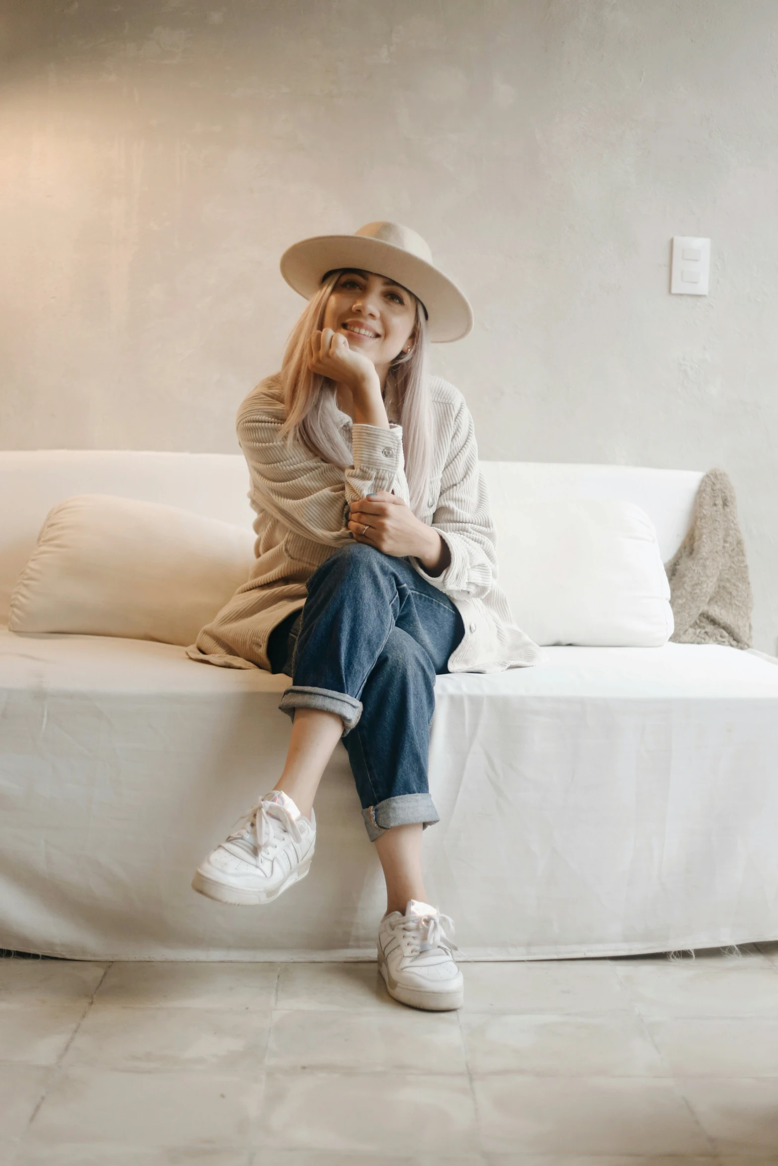 a woman sitting on top of a white couch with her hands resting on her cheek