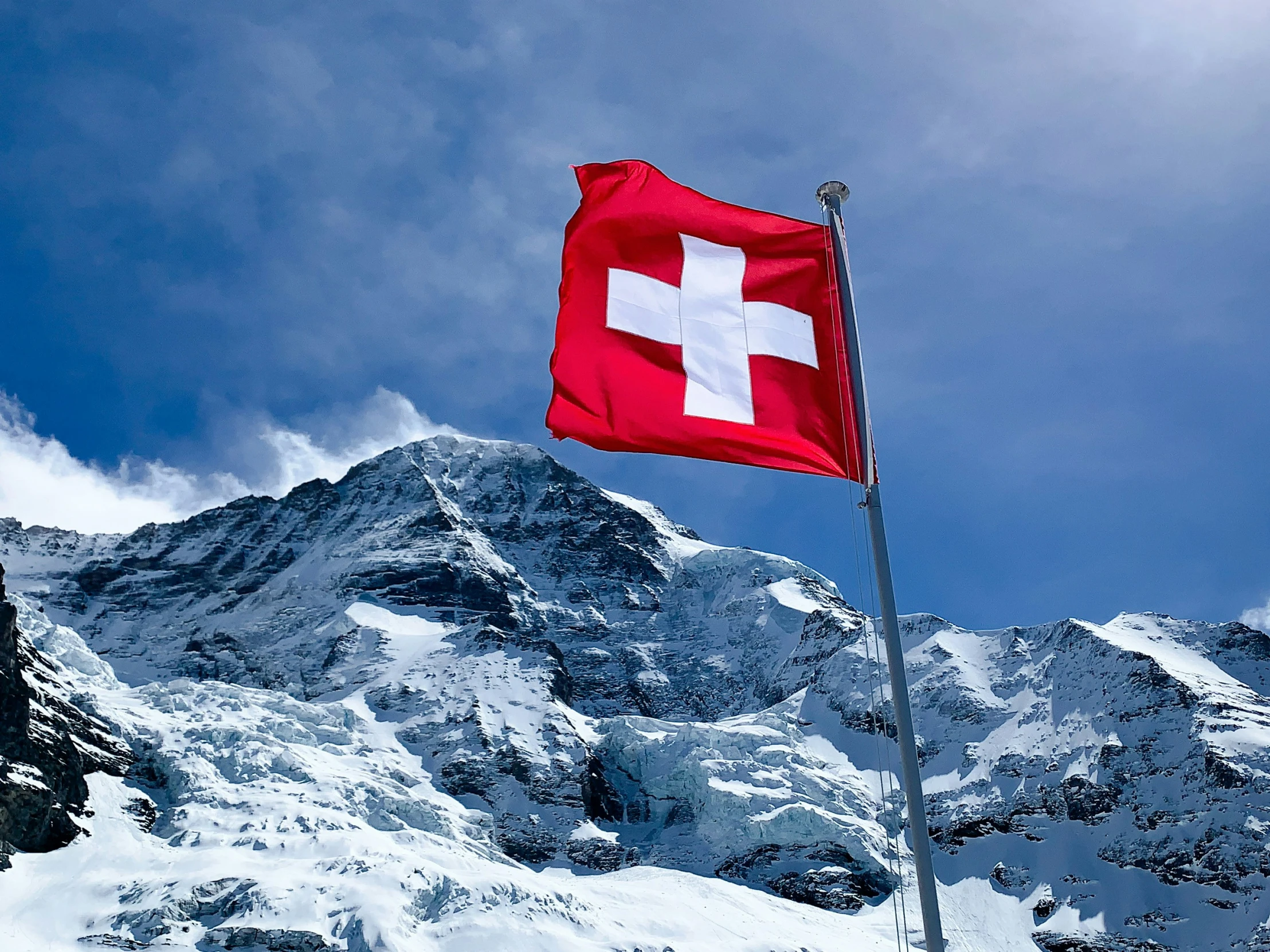 the swiss flag flying high on top of a snowy mountain