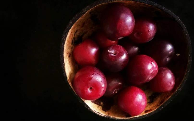 a wooden bowl filled with shiny red fruit