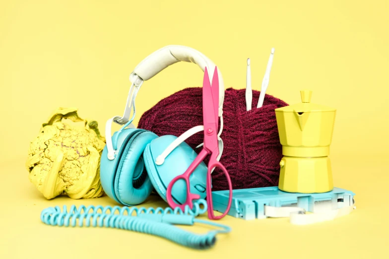 a ball of yarn, a knitting needles and headphones are on the yellow floor