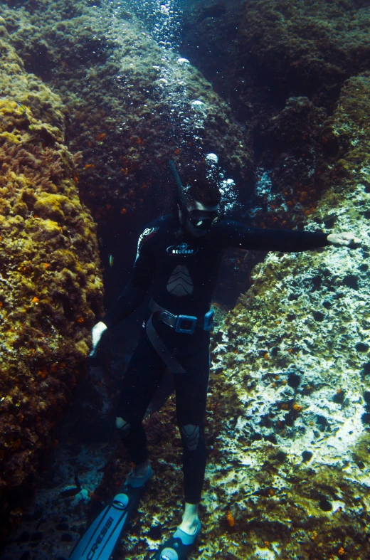 a man with a body board dives through water near large rocks