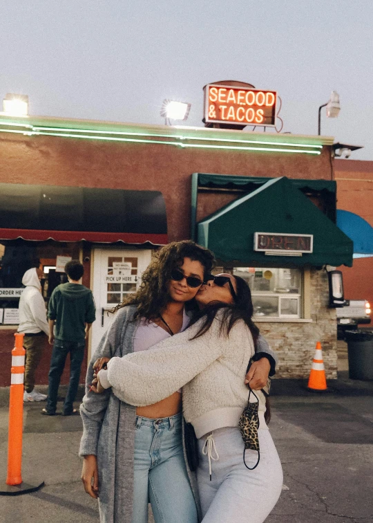 two women hugging in front of the seafood and tacos