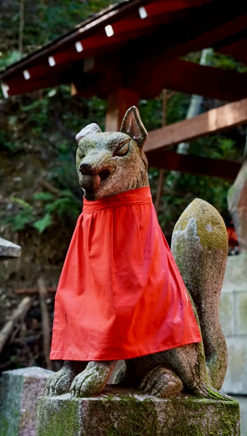 a small squirrel statue is dressed up in a red cape