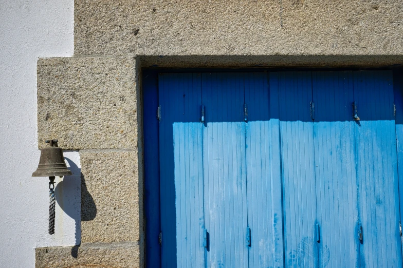 a bell sits on the side of a wall beside a blue door