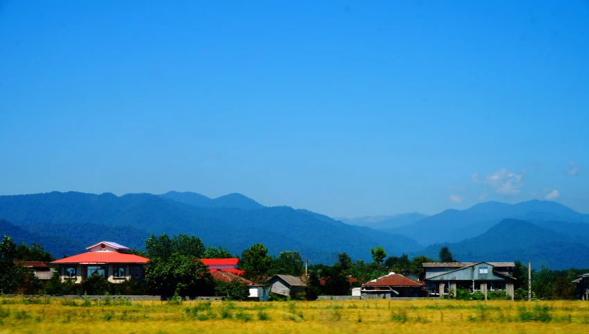a field with houses in the background and mountains in the distance