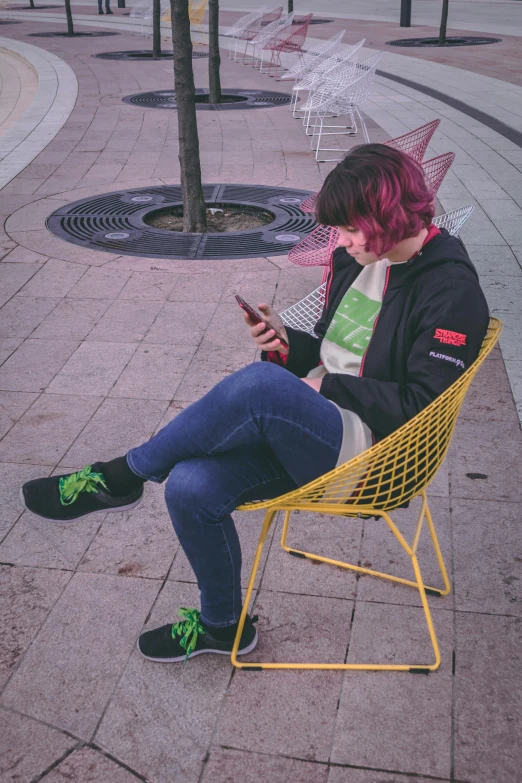 a girl with red hair wearing a jacket and a pair of socks sitting in a chair looking at her phone