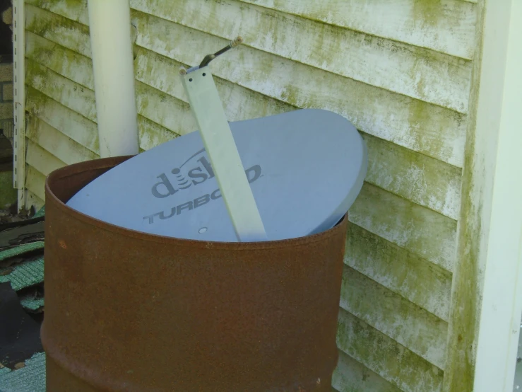 a rusted metal trash can in front of a house with a tag and light pole