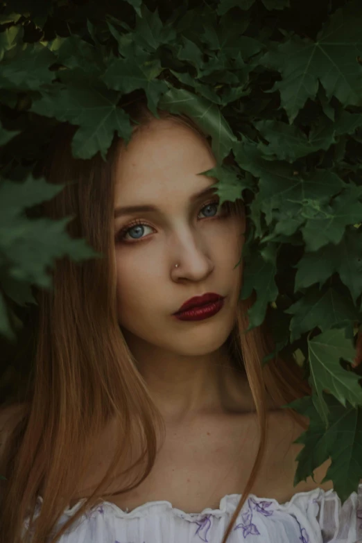 woman with red lipstick staring at camera surrounded by greenery