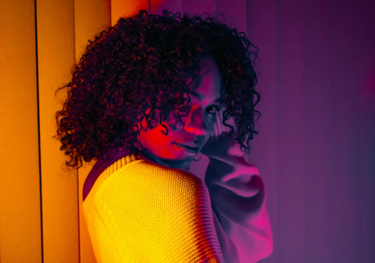 a woman in a bright sweater standing against a wall