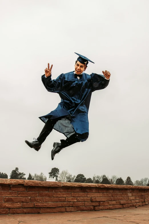 a man dressed in a blue graduation gown is jumping into the air