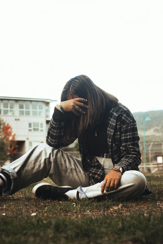 a young person sitting in the grass with a cell phone