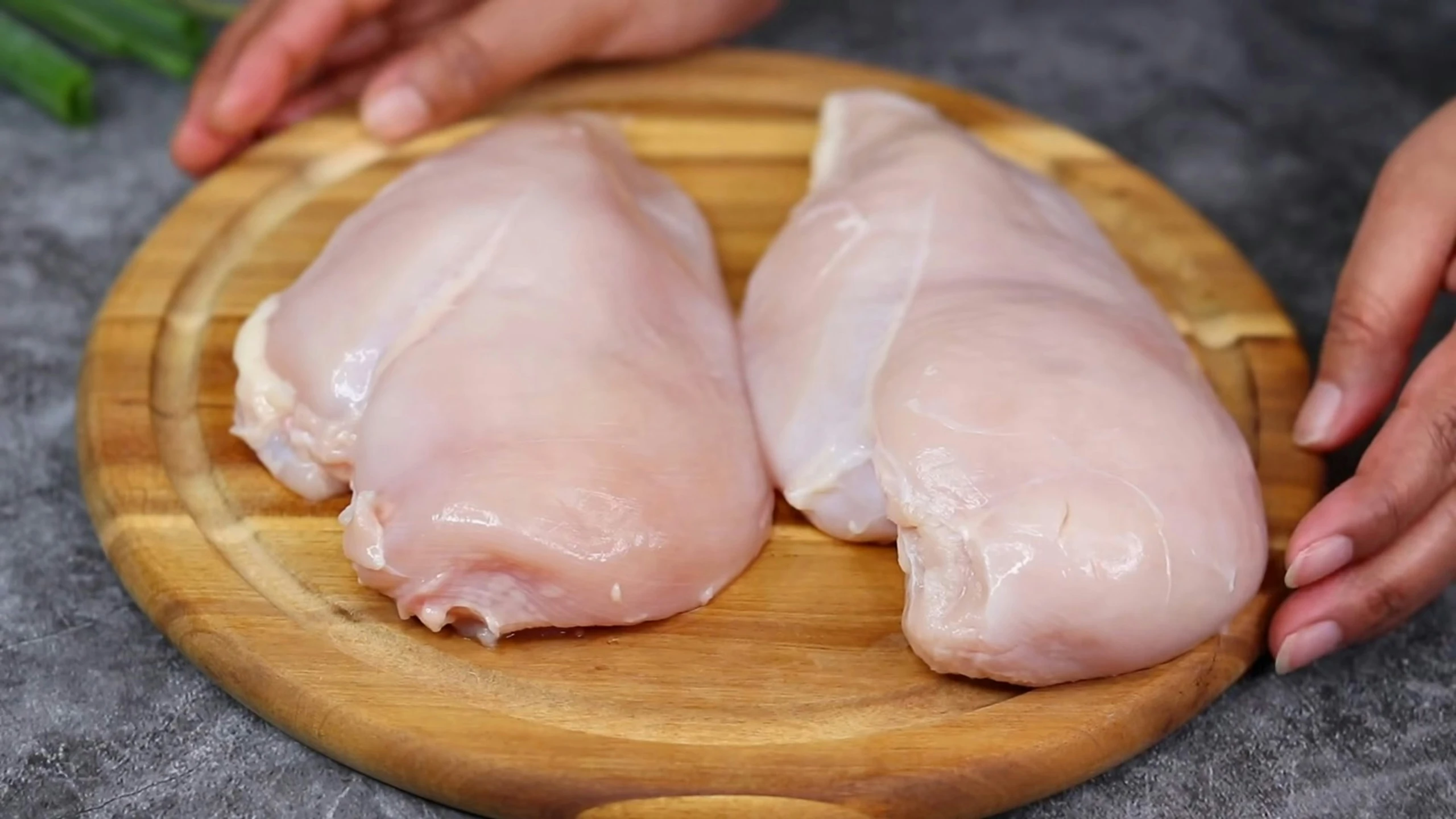 two hands hold raw chicken on a  board