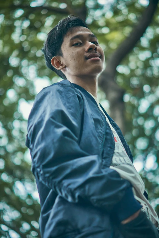 a man wearing a blue jacket standing in front of a tree