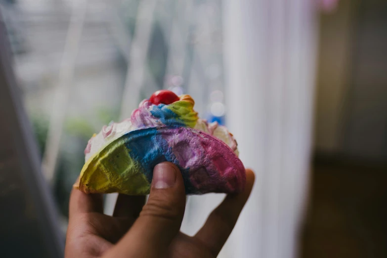 a person holds a small colorful cupcake with cream filling