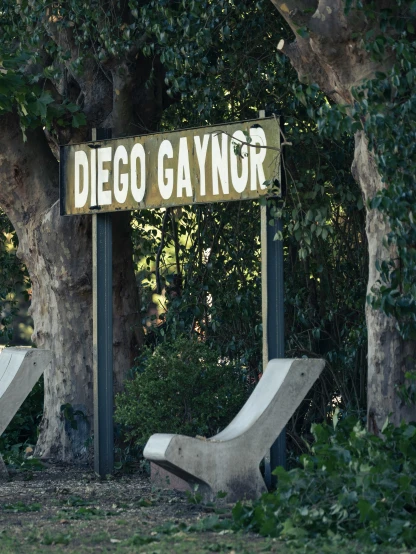 an old sign sits under some trees near some chairs