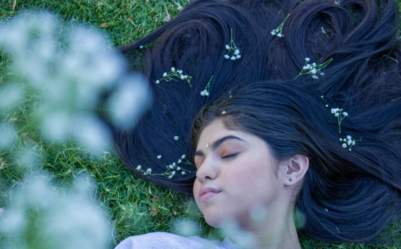 a woman is laying in the grass with her eyes closed and her hair hanging back