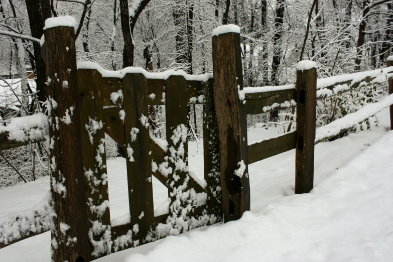 a fence covered in snow next to a forest