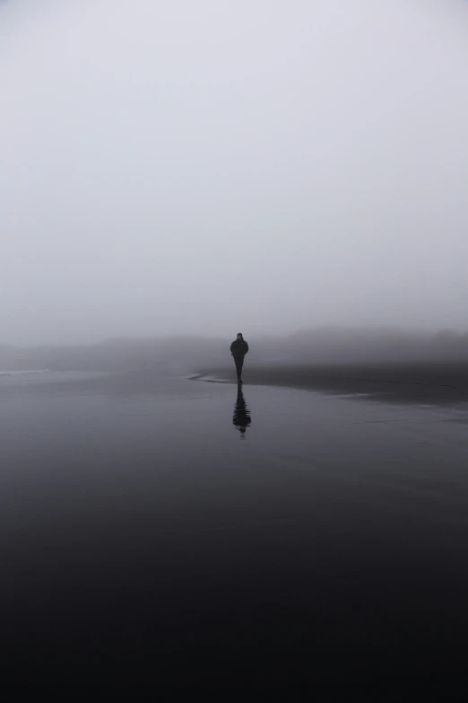 a lone person walks along a beach in the fog