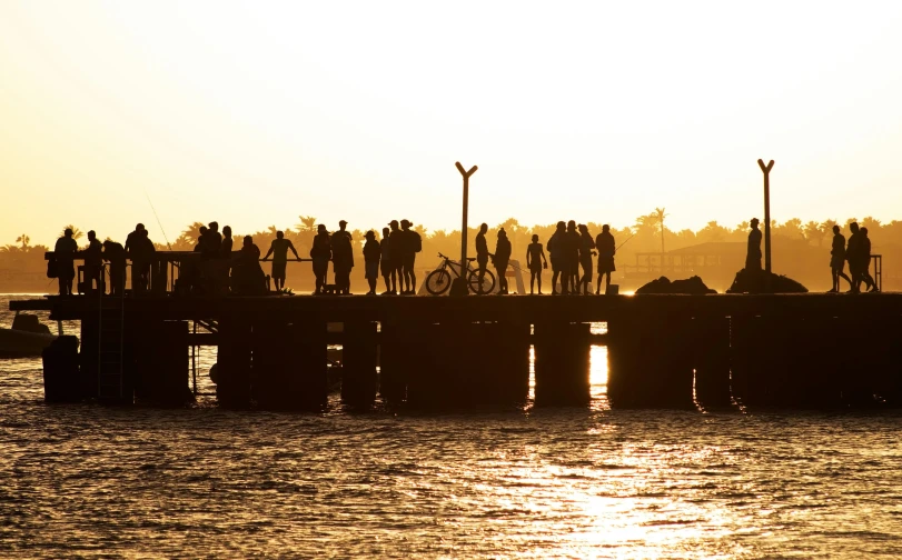 the silhouette of people on the pier in a harbor