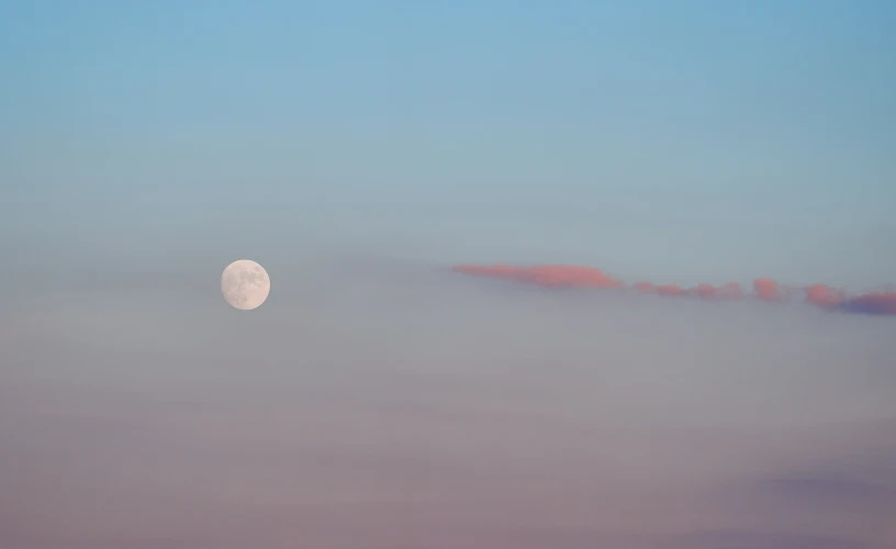 the moon is visible through the foggy blue sky