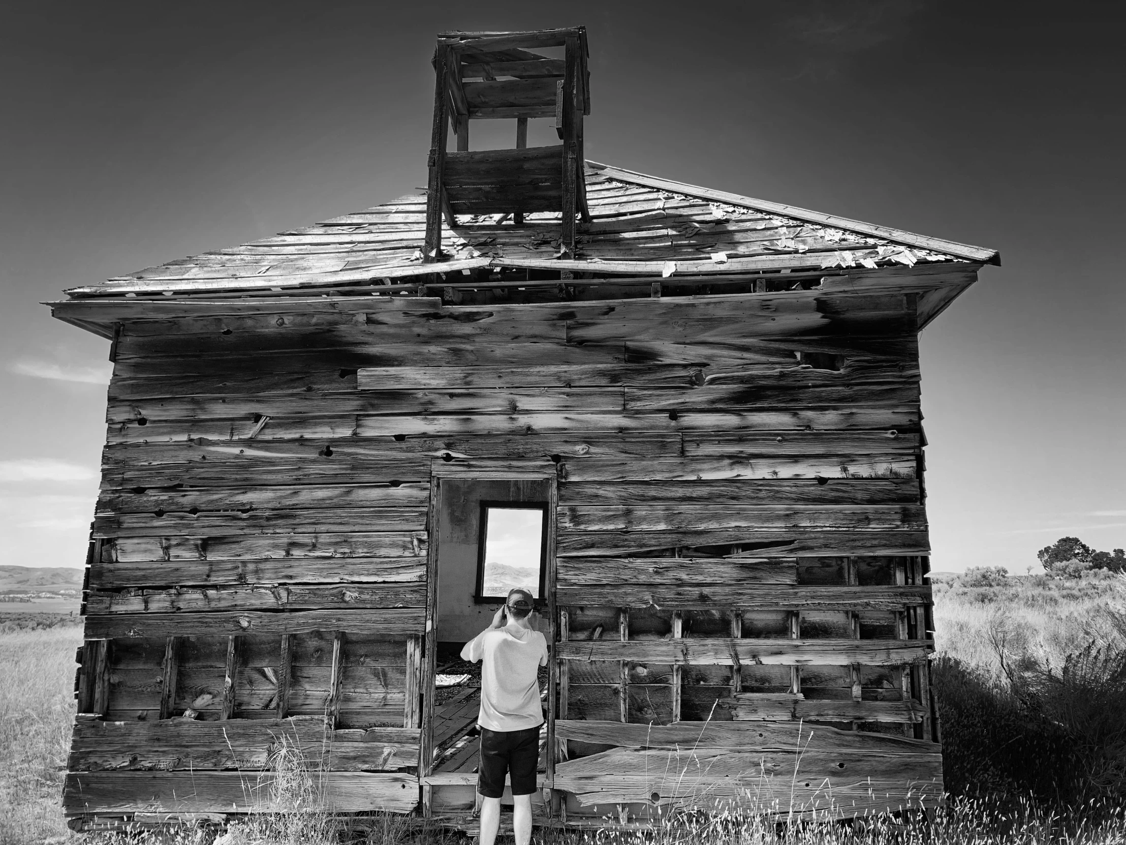 a black and white pograph of a man standing outside a wooden building