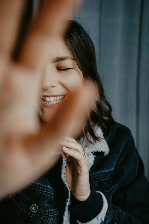 woman smiling and making hand gesture with black jacket