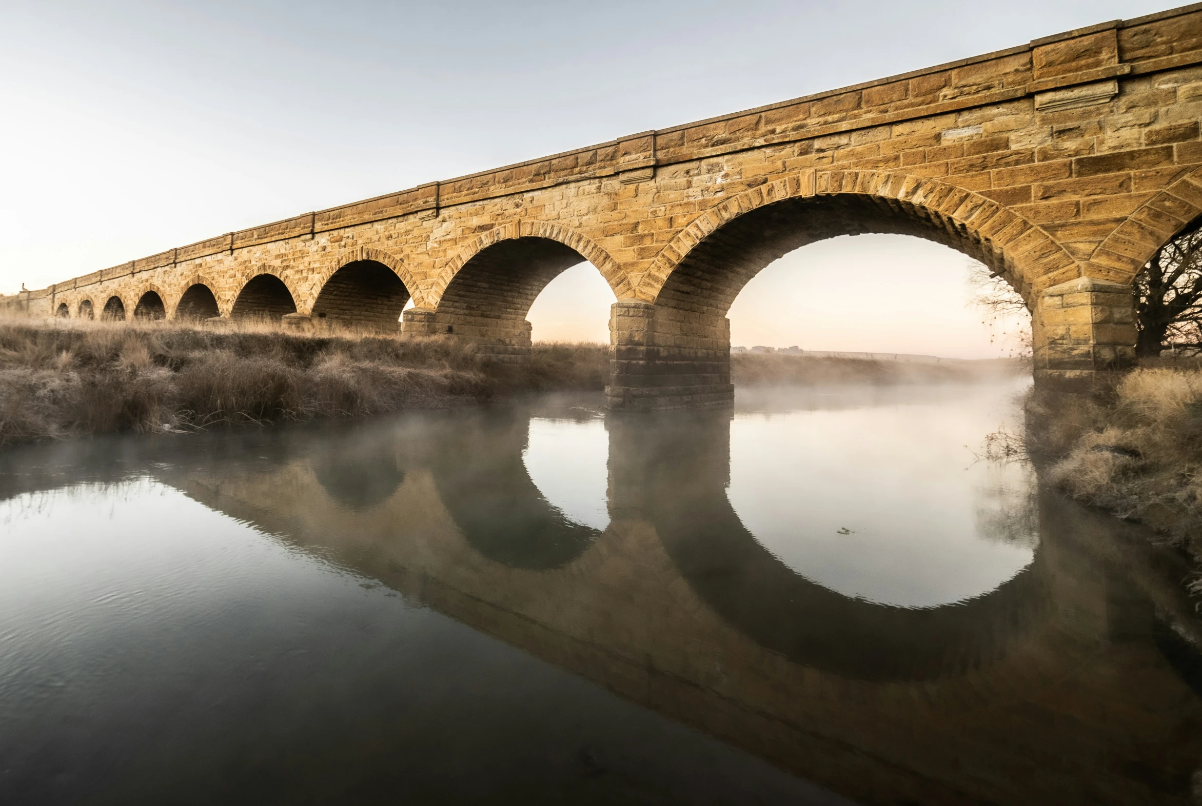 stone arch bridge reflected in water near grass