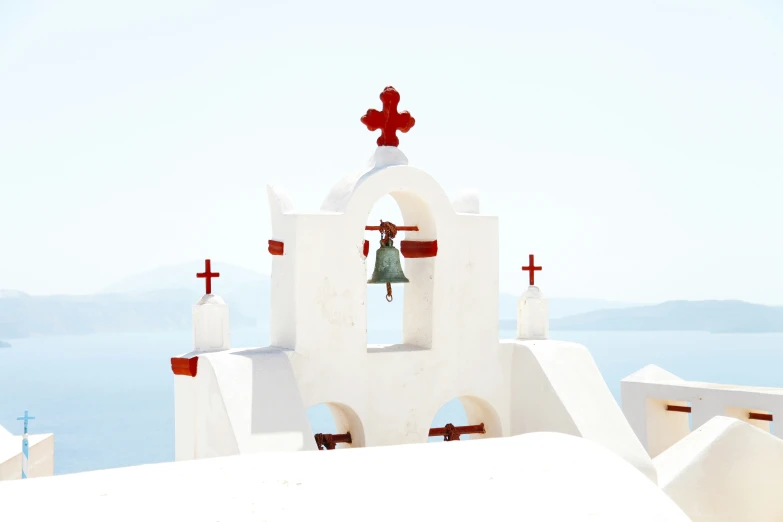 a bell on the top of a white building with red crosses on it