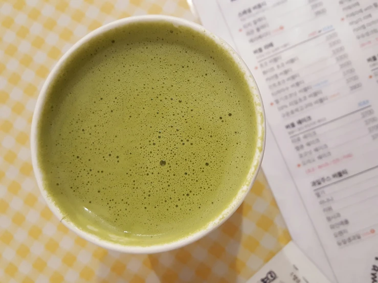 a green liquid in a white bowl sitting on top of a yellow checked table cloth