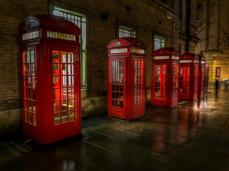 four red phone booths lined up outside the entrance to a building