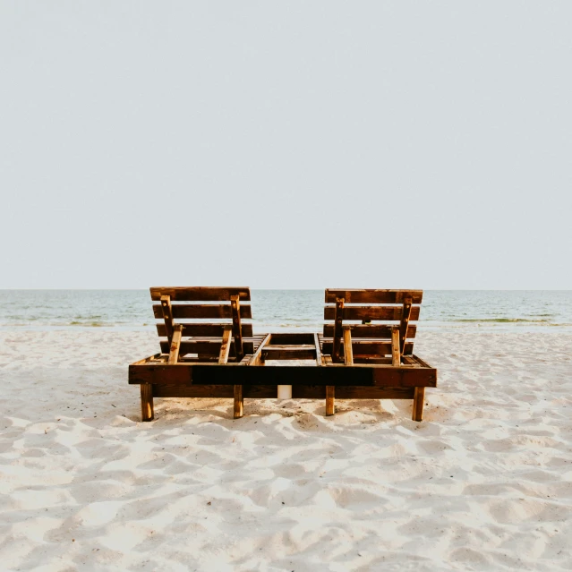 two empty wooden chairs sitting on top of a sandy beach