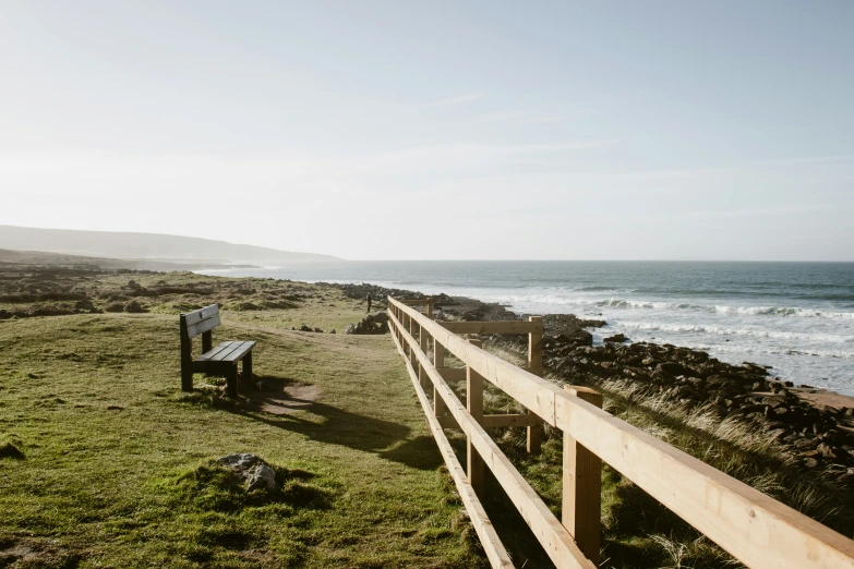 there is an empty bench next to a wooden rail near the ocean