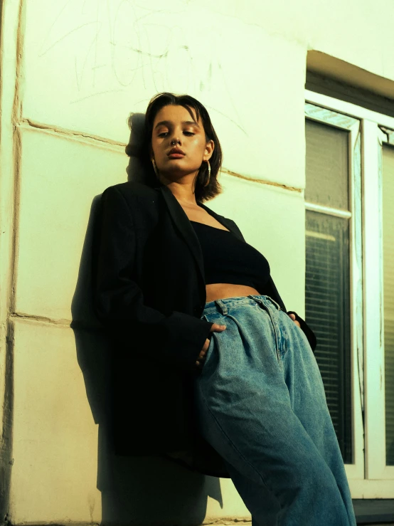 a woman leaning against a wall, wearing jeans