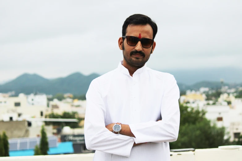 a man in a white shirt and sunglasses standing with his arms crossed and his eyes open