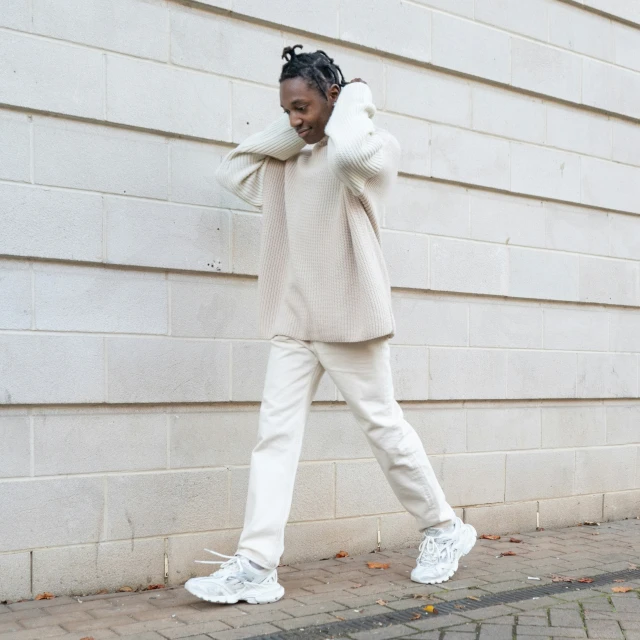 a young woman standing on the sidewalk in her knitted sweater and white pants