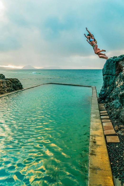 a man diving into a long, green pool next to the ocean