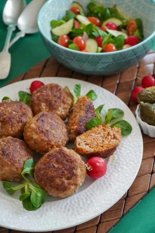 some small meats on a plate next to a bowl of salad