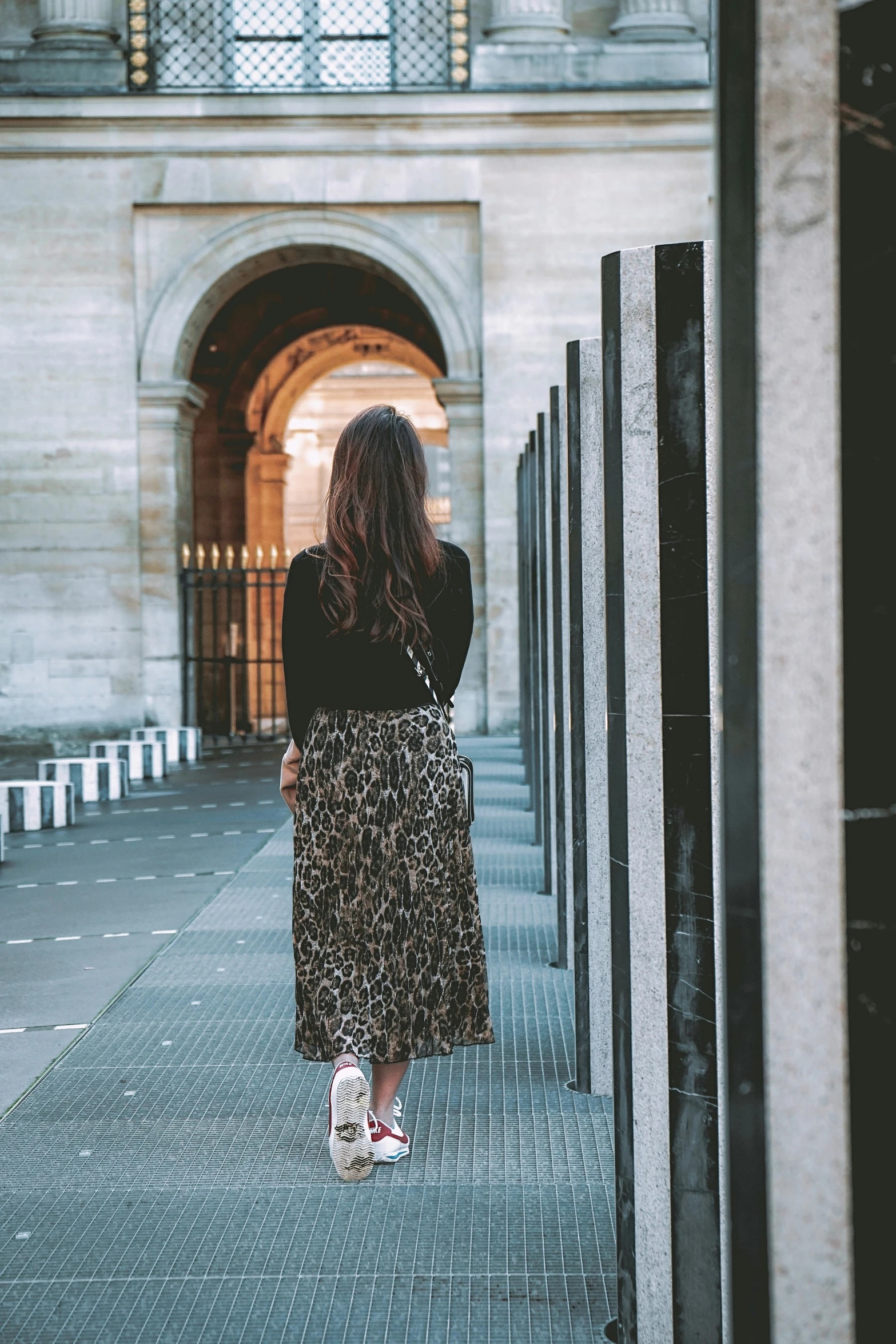 a woman in a leopard print skirt and tennis shoes walking down an alley