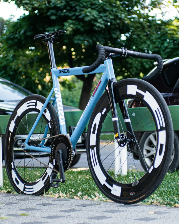 a blue bicycle with white stripes is parked next to two cars