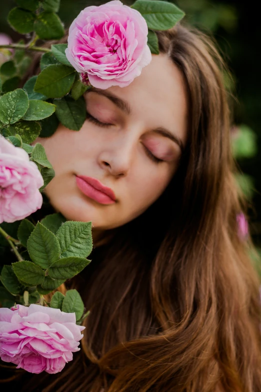 a woman with her eyes closed is smelling the pink roses